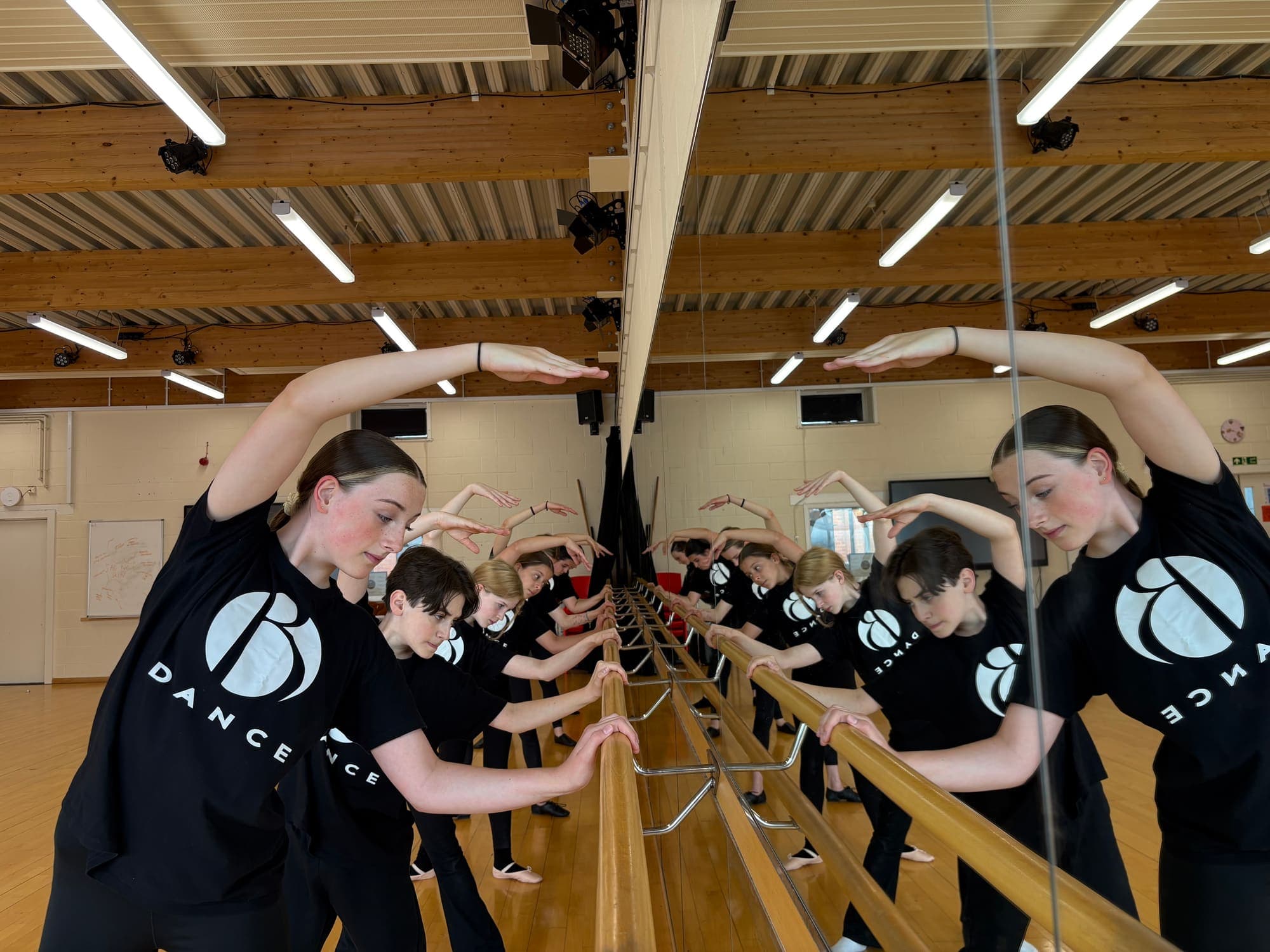 Dancers stretching over the barre, reflected in the studio mirror