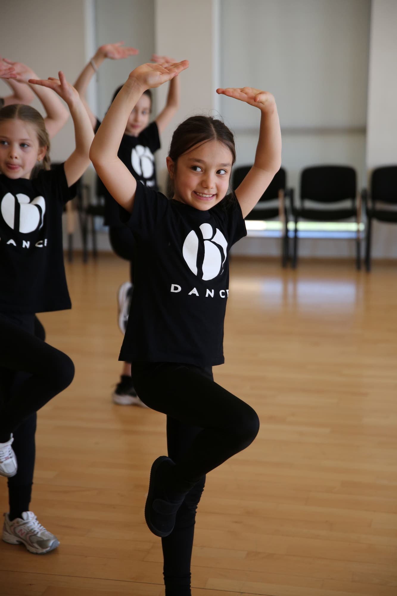 Smiling junior dancers holding their arms in a curve overhead